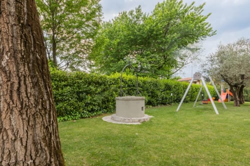 Ampio giardino dell'Hotel Prince Garda con grande albero, altalena, pozzo e verdeggianti spazi verdi a Serniga