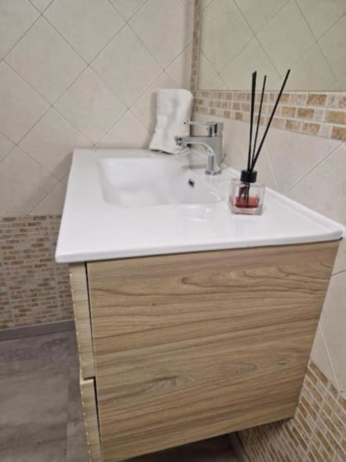 Moderno lavabo del bagno con bacino in ceramica bianca, rubinetto cromato, mobile in legno e diffusore di profumo a Casa Mia Vacanza