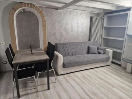 Soggiorno moderno della Living Milano Suite presso Casa Mia Vacanza con divano grigio, tavolo da pranzo, scaffalature e alcova in mattoni ad arco