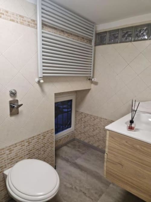 Bagno moderno in appartamento Casa Mia Vacanza Milano con toilette bianca, mobile lavabo in legno, scaldasalviette e dettagli in mattoni