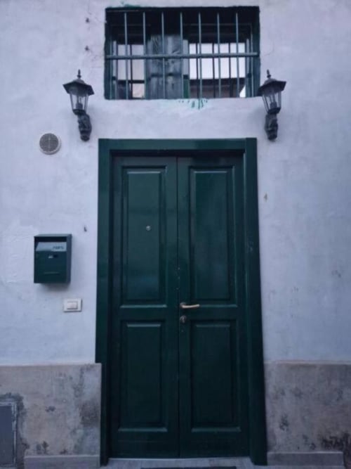 Doppio portone verde con finestra blindata, lanterne e cassetta postale su muro bianco della Milano Suite