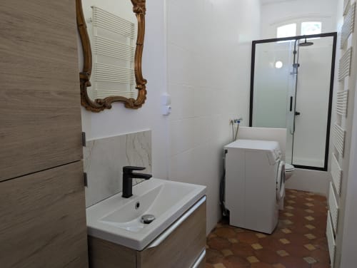 Salle de bain moderne du Gîte Le Chêne avec douche à encadrement noir, lavabo blanc, machine à laver et porte-serviettes chauffants au Domaine du