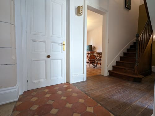 Élégant couloir du Domaine du Faure avec carrelage en terre cuite, portes blanches en bois, escalier en bois et salle à manger