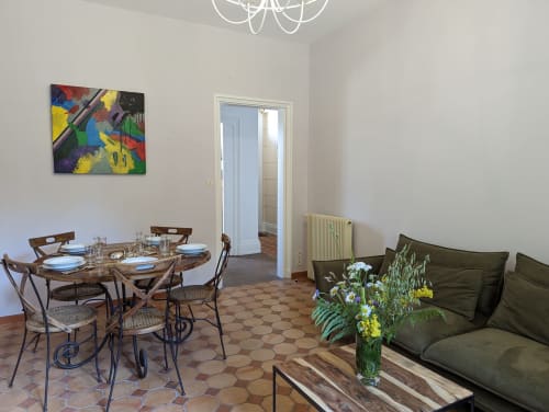 Spacieuse salle à manger et séjour du Gîte Le Chêne au Domaine du Faure avec table en bois, canapé vert et œuvres d'art colorées