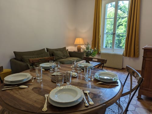 Élégante salle à manger du Domaine du Faure avec table ronde, canapé vert, vue sur le jardin par grandes fenêtres, ambiance chaleureuse