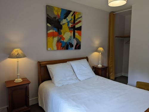 Chambre lumineuse du Domaine du Faure avec lit en bois, linge blanc, art abstrait, lampes de chevet et accès à la vue sur jardin