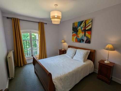 Chambre lumineuse au Domaine du Faure avec lit en bois, vue sur le jardin, rideaux dorés et œuvres d'art colorées
