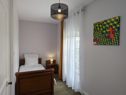 Chambre douillette au Domaine du Faure avec lit en bois, luminaire suspendu, draps blancs et œuvres d'art abstraites colorées à Chadurie.
