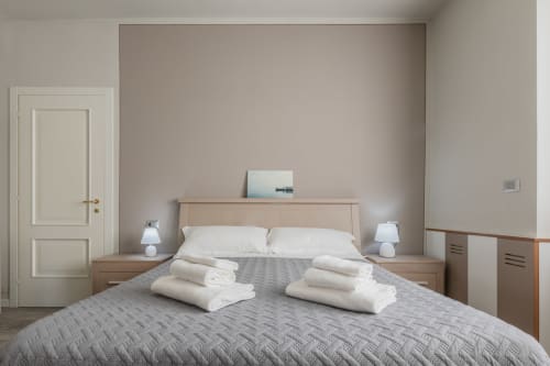 Camera da letto dell'Hotel Prince Garda a Serniga con letto matrimoniale, cuscini bianchi, coperta trapuntata grigia e comodini in legno