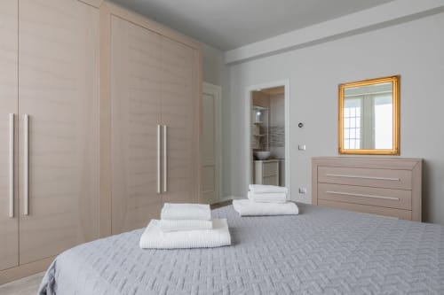Camera moderna dell'hotel Prince Garda a Serniga con armadio in legno beige, letto grigio, asciugamani bianchi e specchio con cornice dorata