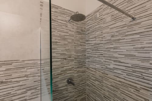 Moderna cabina doccia dell'hotel Prince Garda a Serniga con pareti rivestite di piastrelle a righe e soffione pioggia