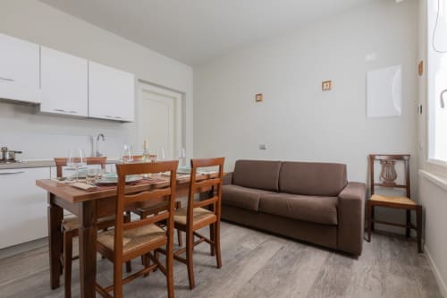 Soggiorno e cucina a open space dell'hotel Prince Garda a Serniga con tavolo da pranzo in legno, divano marrone e arredi moderni bianchi