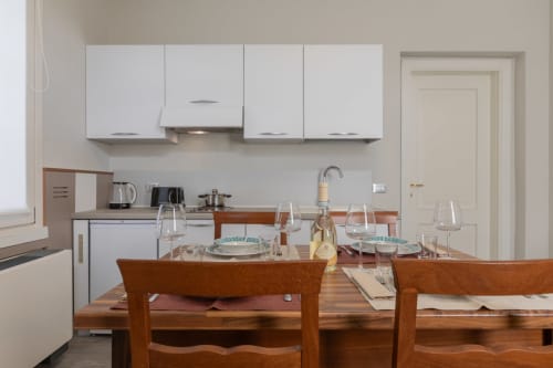 Elegante zona pranzo con tavolo e sedie in legno presso l'hotel Prince Garda di Serniga, con vista sulla cucina moderna bianca