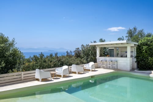 Luxury villa in Sardinia with turquoise pool, white lounge chairs, bar, and Mediterranean sea view