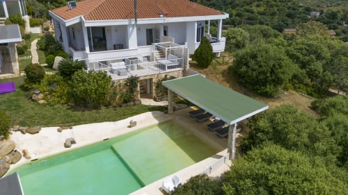 Modern white villa with terracotta roof, green pool, pergola, and lounge chairs in Sardinia