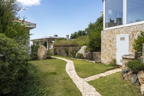 Stone villa garden with paved pathway, green lawn, and Mediterranean landscaping at Top Villas Sardinia, Quartu Sant'Elena