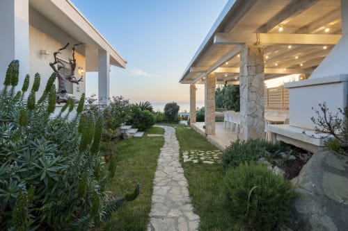 Luxury villa pathway with stone patio, modern pergola, and Mediterranean gardens at sunset in Sardinia