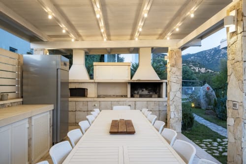 Modern outdoor dining area at Top Villas Sardinia with long table, white chairs, built-in kitchen, and mountain views in