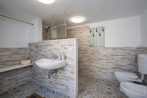 Modern bathroom with warm tile backsplash, wall-mounted sink, mirror, and toilet at Top Villas Sardinia in Quartu Sant'Elena