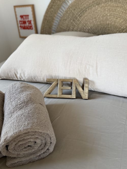 Serviette roulée et oreiller blanc sur le lit du Petit Coin de Paradis à Alata avec une pancarte en bois « ZEN »