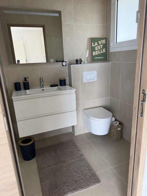 Salle de bain moderne du gîte Petit Coin de Paradis à Alata avec meuble vasque blanc, toilettes et carrelage beige