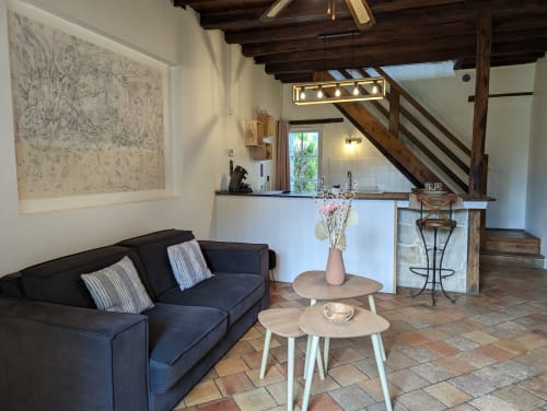 Coin séjour douillet du gîte Le Rose au Domaine du Faure avec canapé sombre, tables en bois et escalier