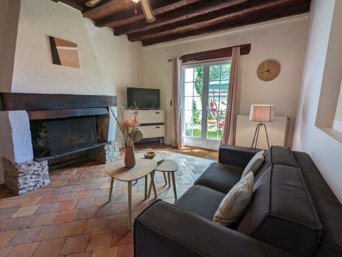 Salon cosy du Domaine du Faure avec canapé sombre, cheminée, carrelage en terre cuite et vue sur le jardin