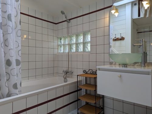 Salle de bain moderne du Gîte Le Rose au Domaine du Faure avec carrelage blanc, douche vitrée, lavabo vert et vue sur le jardin