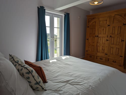 Chambre spacieuse du gîte Le Châtaigne avec vue sur le jardin, armoire en bois et rideaux bleus