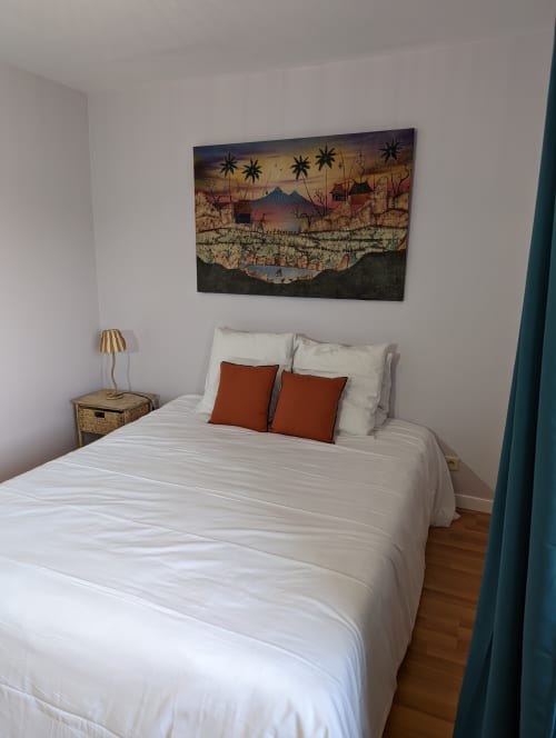 Chambre douillette au Domaine du Faure avec draps blancs, coussins rouille, table de nuit tressée et œuvre d'art paysagère colorée