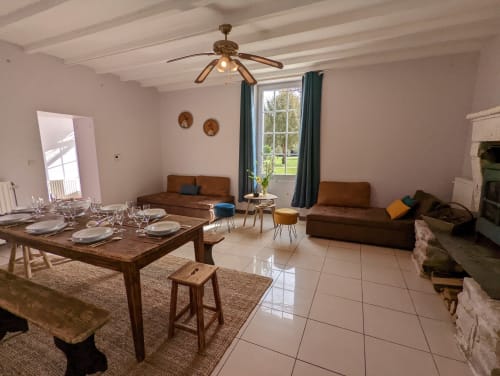 Salon spacieux du Gîte Le Châtaigne avec table à manger, canapés marron, ventilateur de plafond et vue sur le jardin