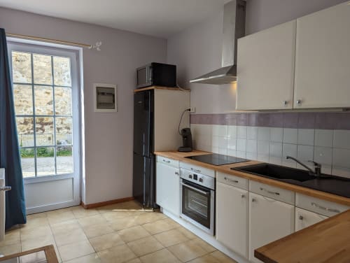 Cuisine moderne au gîte Le Châtaigne du Domaine du Faure, avec meubles blancs, plans de travail noirs et carrelage