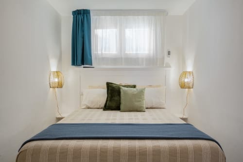 Modern bedroom at Top Villas Sardinia with white headboard, green pillows, woven lamps, and teal curtains in Quartu