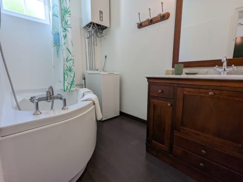 Salle de bain élégante du Gîte Le Bambou au Domaine du Faure avec baignoire arrondie, meuble-lavabo en bois et vue sur le jardin.