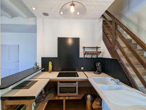 Cuisine moderne avec crédence noire, plaque à induction, évier blanc et escalier en bois au Gîte Le Bambou du Domaine du Faure