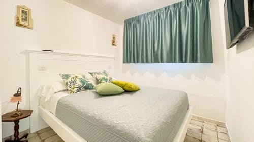 Modern bedroom at Top Villas Sardinia with white bed, green pillows, and curtained window in Quartu Sant'Elena