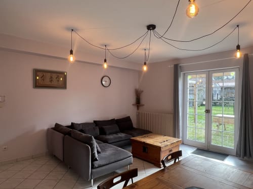 Séjour contemporain du Gîte Le Prune avec canapé gris, table en bois, luminaires suspendus et vue sur le jardin