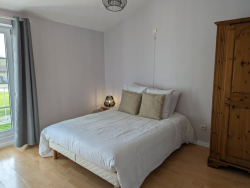 Chambre lumineuse avec lit blanc, armoire en bois et vue sur le jardin au gîte Domaine du Faure à Chadurie