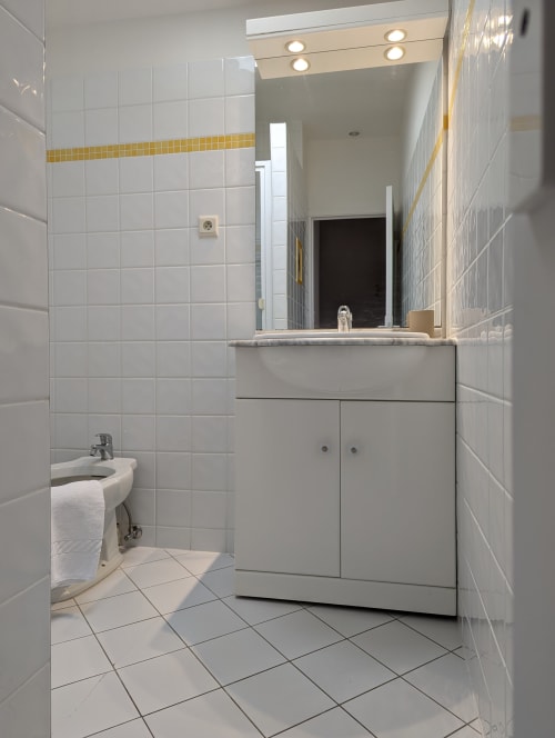 Salle de bain moderne avec carrelage blanc, liseré jaune, meuble vasque et miroir au gîte Domaine du Faure