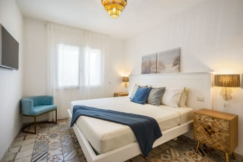 Elegant bedroom at Top Villas Sardinia with white bed, blue accents, gold fixtures, and patterned floor in Quartu Sant'Elena