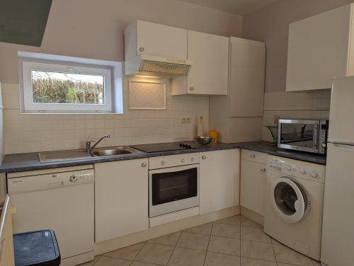 Cuisine crème avec placards beige, plan de travail noir, four, lave-linge et vue sur le jardin au Domaine du Faure
