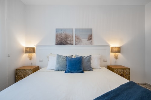 Modern bedroom at Top Villas Sardinia with white bedding, blue pillows, wood nightstands, and coastal wall art
