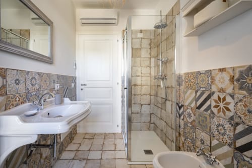 Modern bathroom at Top Villas Sardinia with patterned tile walls, white sink, walk-in shower, and overhead rainfall