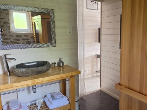 Salle de bains moderne avec vasque en pierre, meuble de rangement en bois, miroir encadré et porte de sauna privatif à l'hôtel Les Instants Volés