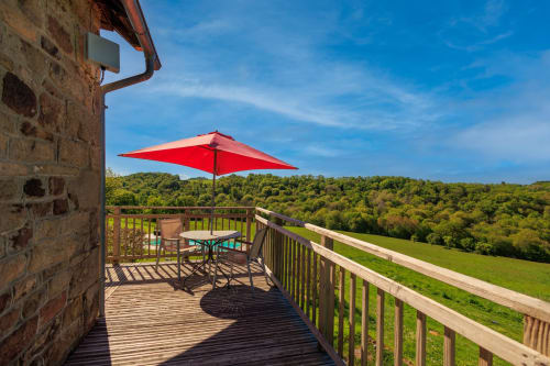 Parasol rouge et chaise sur balcon en bois surplombant une vallée verdoyante aux Instants Volés, Tudeils