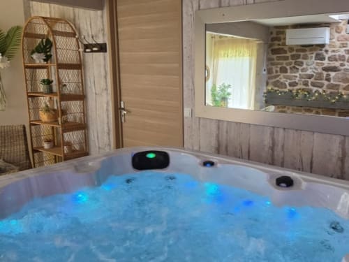 Baignoire à remous luxueuse et illuminée dans la chambre Les Instants Romantiques à Les Instants Volés, Tudeils, murs en pierre et design contemporain