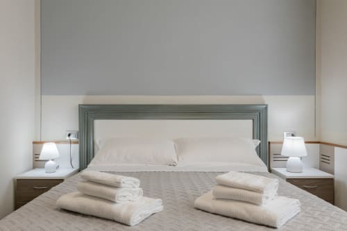 Camera moderna dell'hotel Prince Garda a Serniga con asciugamani piegati ordinatamente sul letto, testata verde e lampade laterali