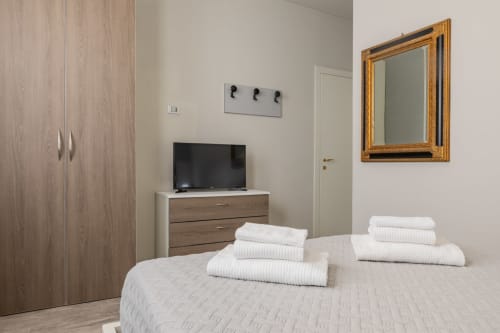 Camera moderna dell'Hotel Prince Garda a Serniga con asciugamani bianchi, TV, specchio e guardaroba in legno