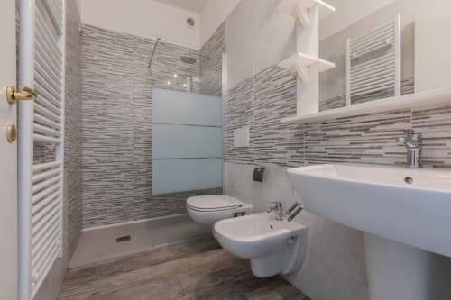 Bagno moderno dell'hotel Prince Garda a Serniga con piastrelle grigie a righe, sanitari bianchi e cabina doccia in vetro