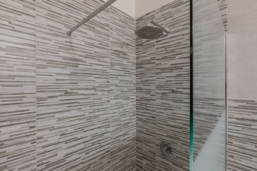 Moderna doccia walk-in con piastrelle grigie a righe e box doccia in vetro all'hotel Prince Garda di Serniga